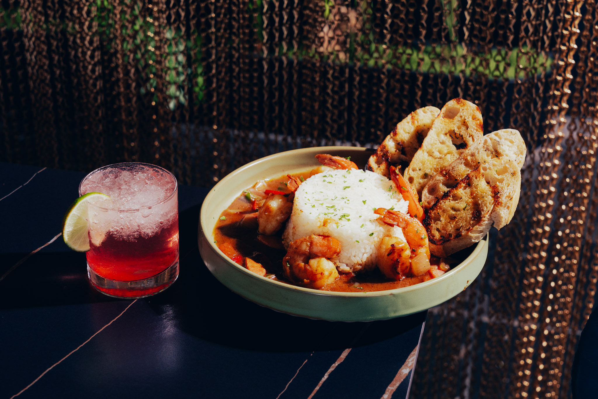 Shrimp rice dish paired with red citrus cocktail on dark table