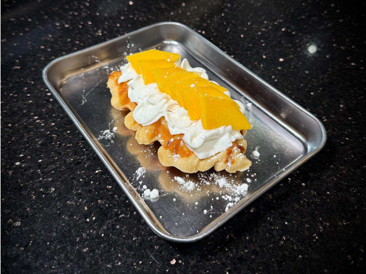 Sweet mango croffle topped with cream and fresh mango slices on tray at 592 Korean BBQ, an Asian Fusion Restaurant in Appleton