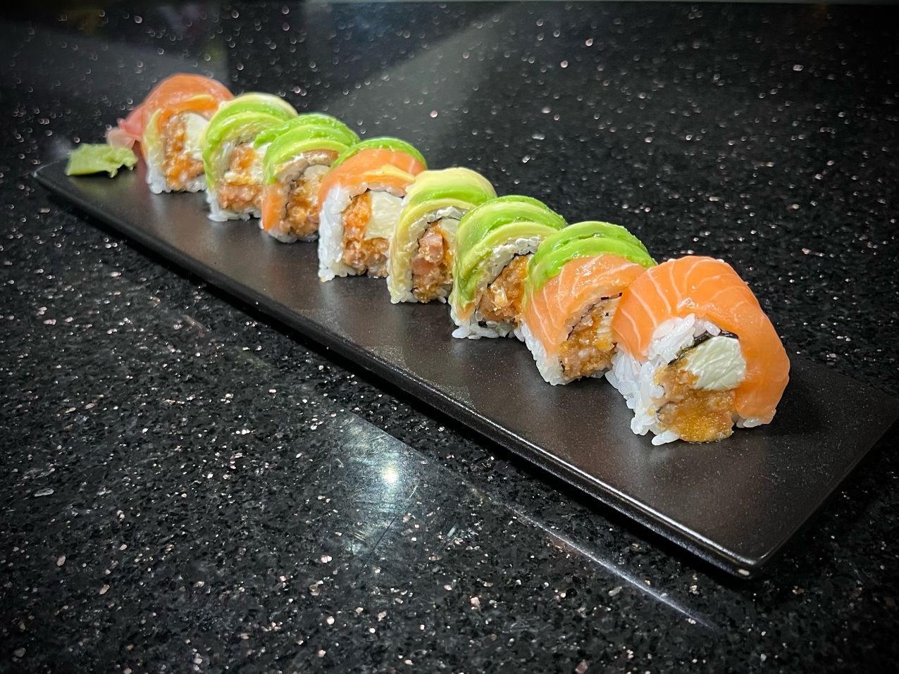 Sake salmon sushi roll with avocado and fresh garnish on black countertop at 592 Korean BBQ, an Asian Fusion Restaurant in Appleton