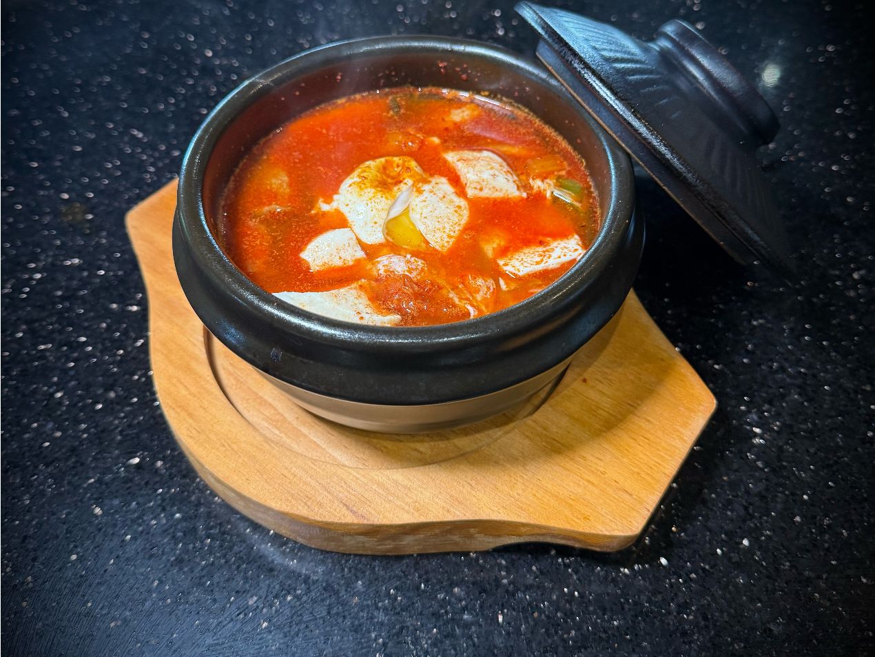 Bowl of boiling spicy seafood soup in hot stone pot with wooden base at 592 Korean BBQ, an Asian Fusion Restaurant in Appleton