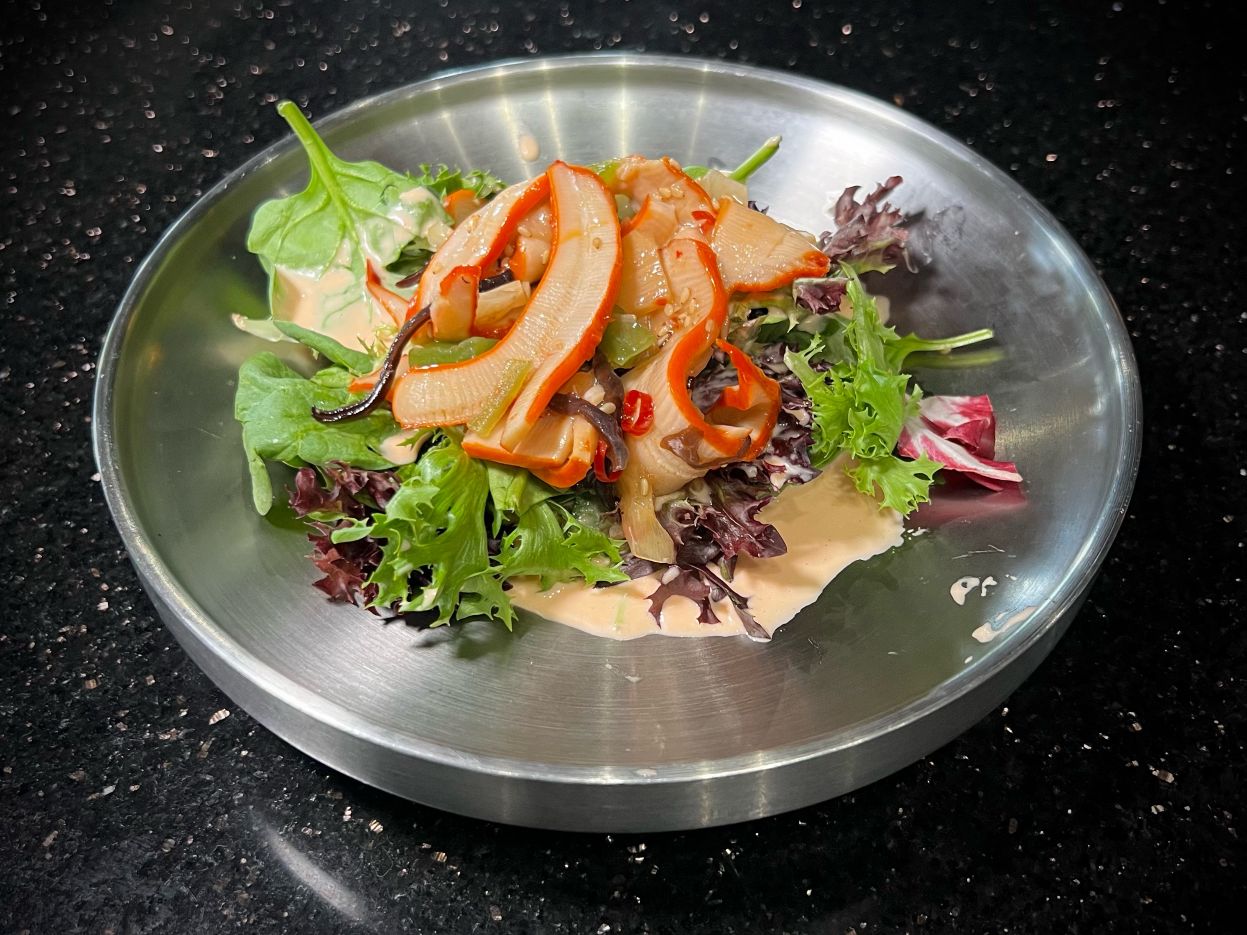 Spicy squid salad mixed with fresh leafy greens on metal round plate at 592 Korean BBQ, an Asian Fusion Restaurant in Appleton