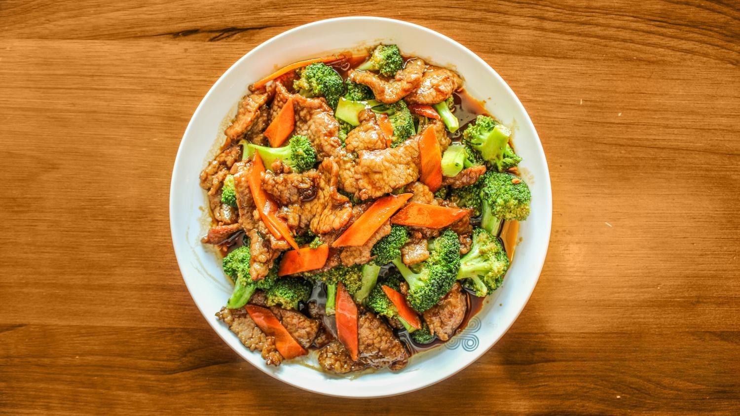 Plate of beef stir-fried with broccoli and carrots in a savory sauce on a wooden table