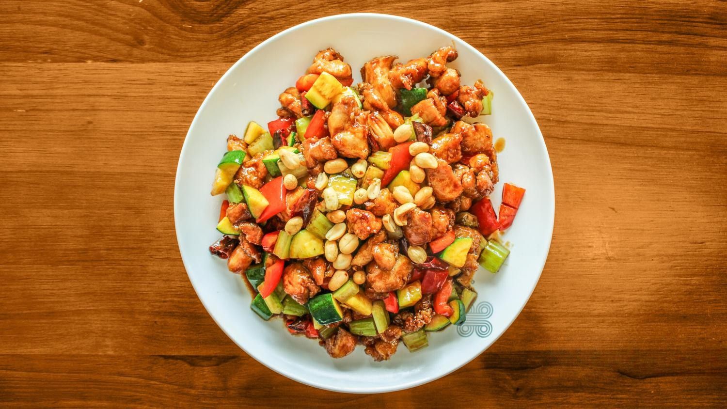 Plate of Kung Pao chicken with peanuts, colorful veggies on a wooden table