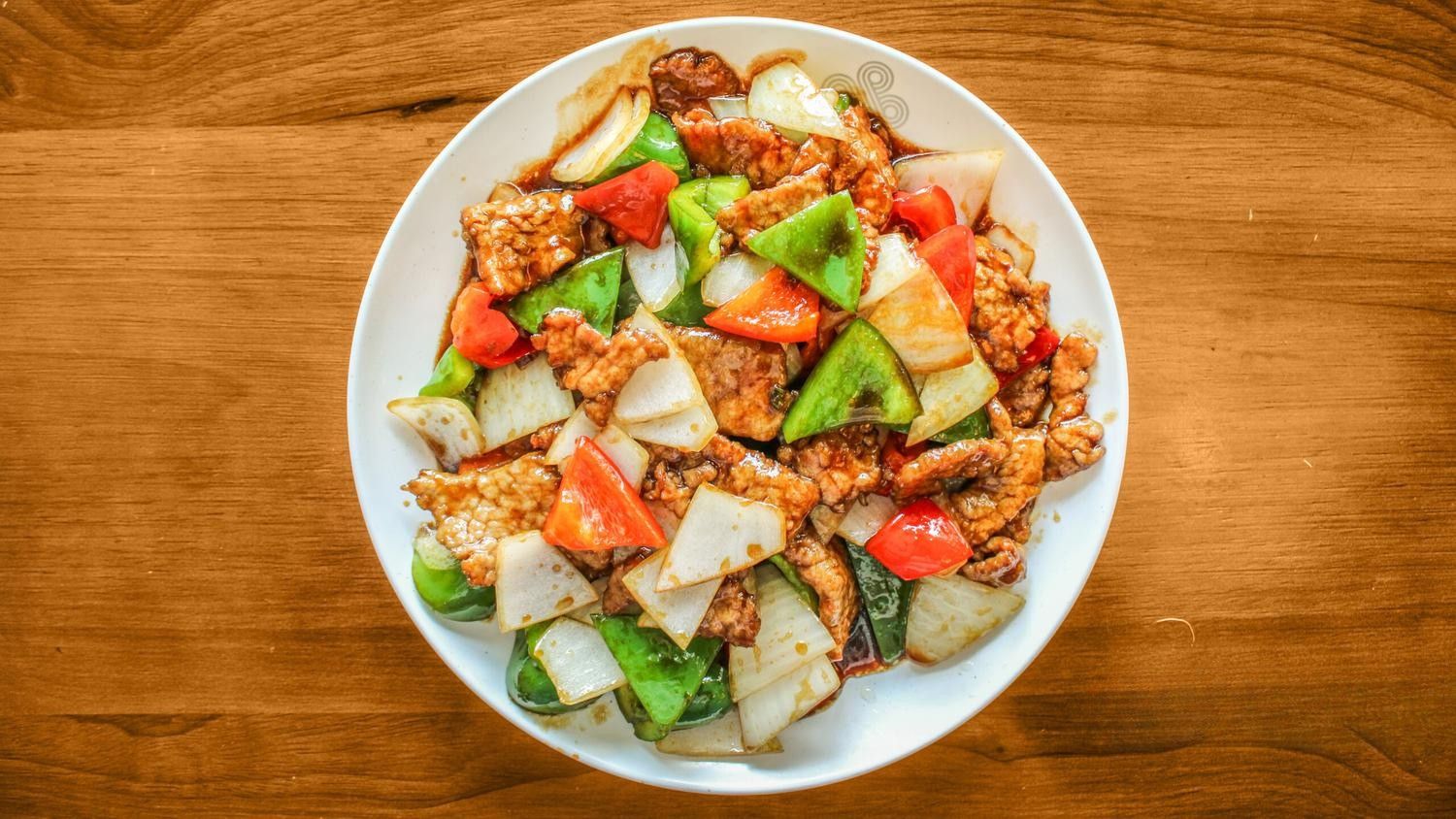 Plate of meat stir-fried with green and red bell peppers, onions on a wooden table