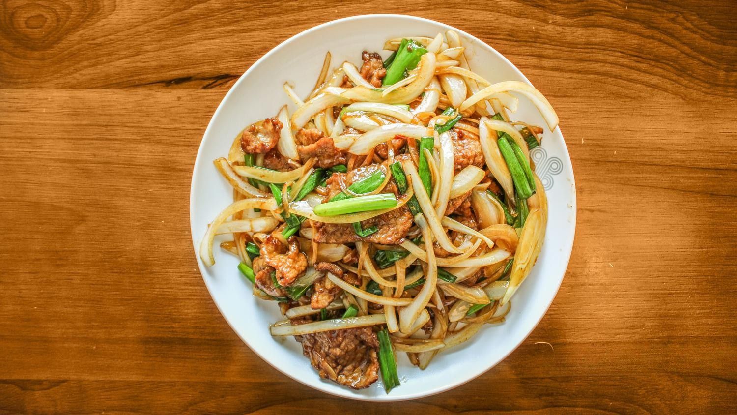 Plate of stir-fried meat with onions and green scallions on a wooden table