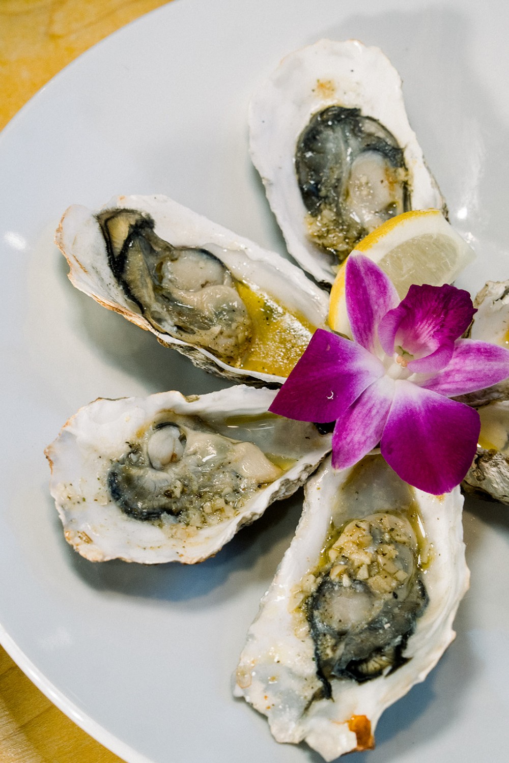 Grilled oysters with garlic butter, lemon and orchid garnish