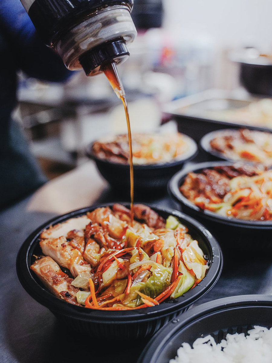 Teriyaki chicken bowl pouring savory sauce over veggies
