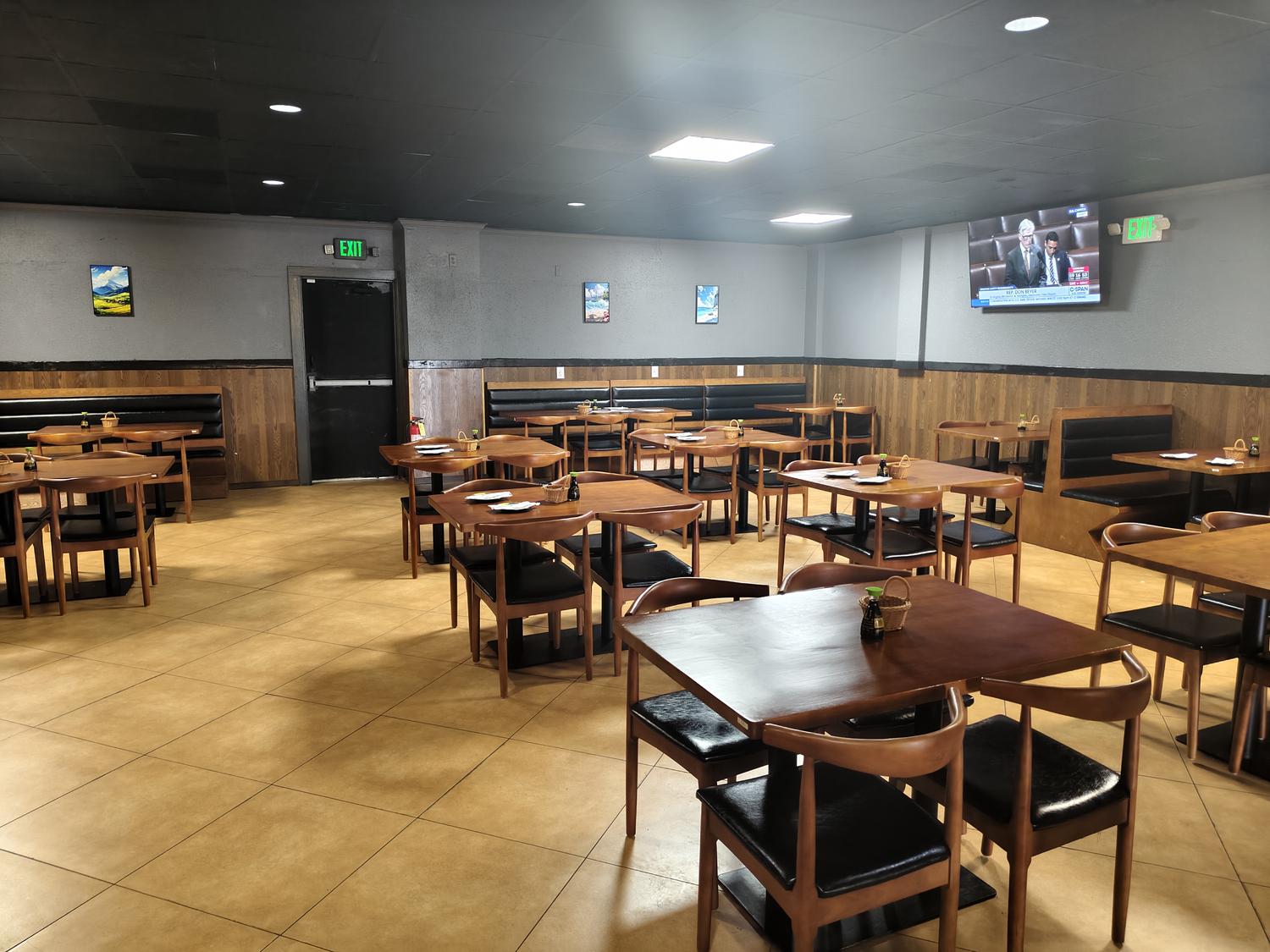 Spacious restaurant dining room with wooden tables, chairs, and a TV mounted on the wall.