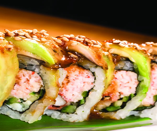 Sliced sushi roll filled with crab, cucumber, topped with avocado, sesame seeds and glossy teriyaki sauce at Akira, a Japanese Restaurant in Glenmont