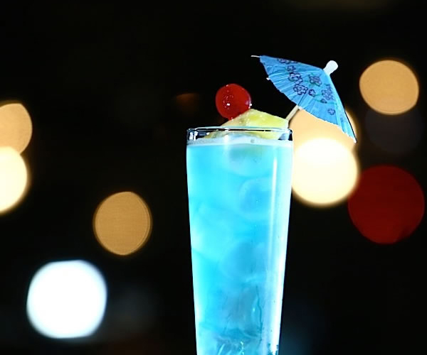 Tall glass of vivid blue cocktail topped with pineapple, cherry and tiny paper cocktail umbrella at Akira, a Japanese Restaurant in Glenmont