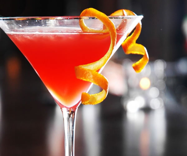 Bright red martini drink garnished with twisted orange citrus peel in clear triangular glass at Akira, a Japanese Restaurant in Glenmont