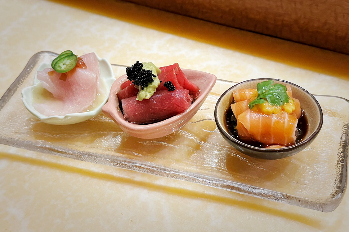 Three small sashimi appetizer portions presented on a long transparent glass serving tray at Aki Sushi & Asian Fusion, a Sushi Restaurant in Port Washington