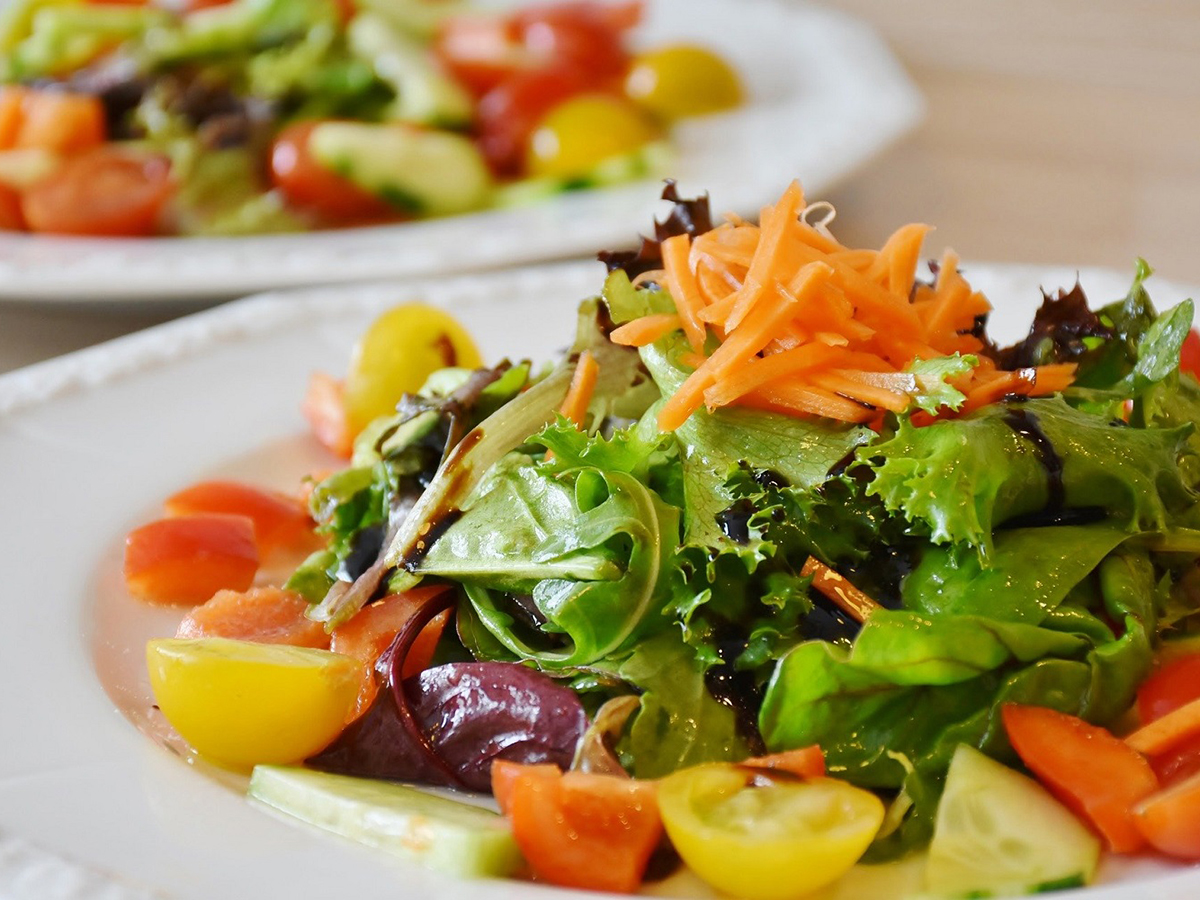 Fresh mixed vegetable salad with tomatoes, cucumber and shredded carrot on white ceramic plates at Aki Sushi & Asian Fusion, a Sushi Restaurant in Port Washington