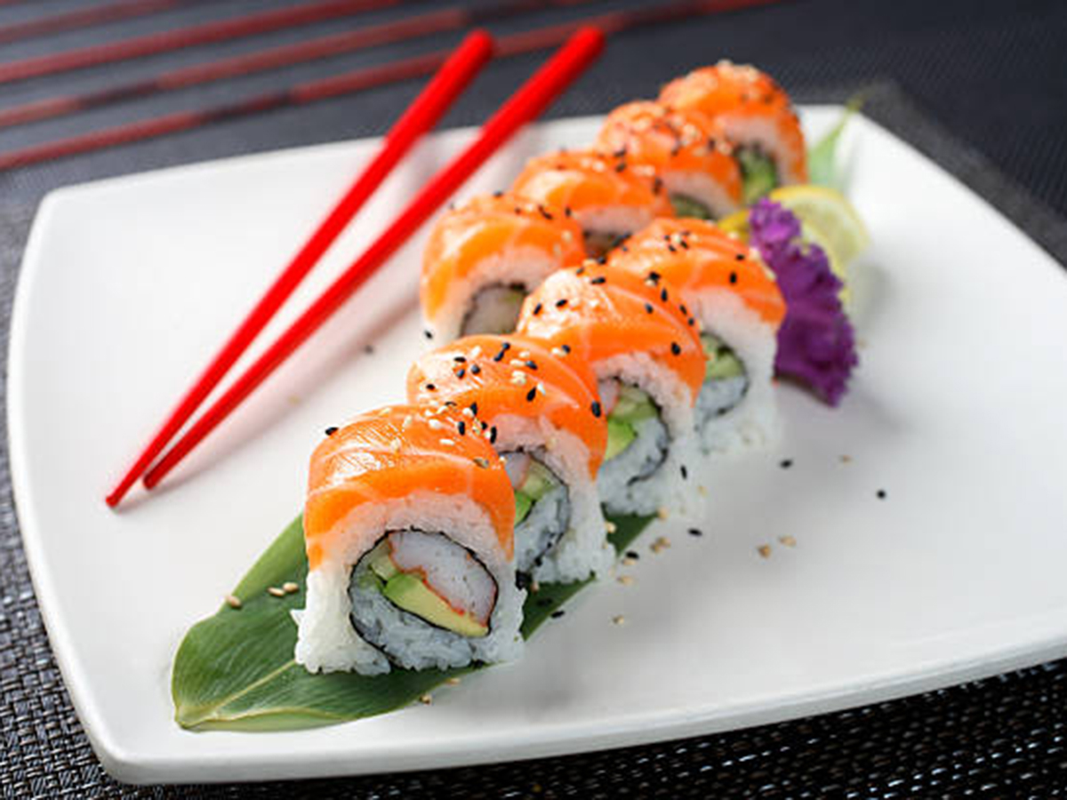 Salmon sushi roll slices garnished with sesame seeds, served with red chopsticks on square white plate at Aki Sushi & Asian Fusion, a Sushi Restaurant in Port Washington