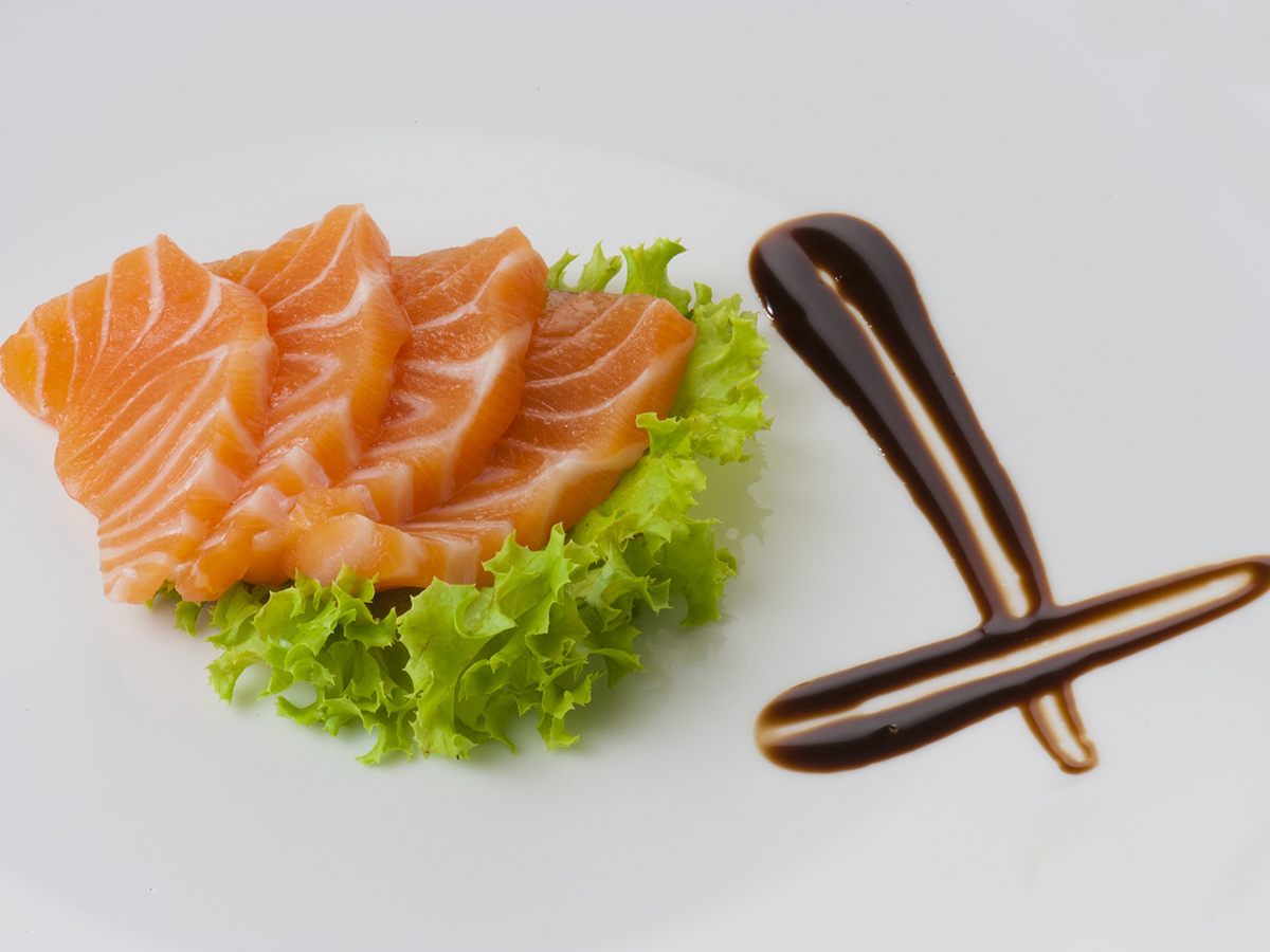 Salmon sashimi slices laid over lettuce, decorated with artistic soy sauce drizzle on white plate at Aki Sushi & Asian Fusion, a Sushi Restaurant in Port Washington
