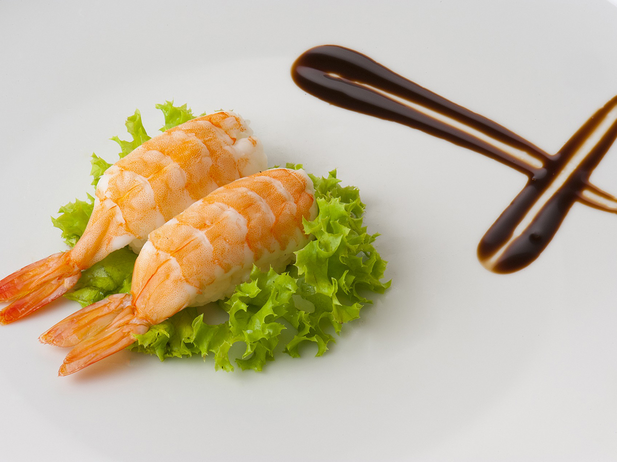 Two pieces of shrimp nigiri sushi with artistic soy sauce decoration on clean white plate at Aki Sushi & Asian Fusion, a Sushi Restaurant in Port Washington
