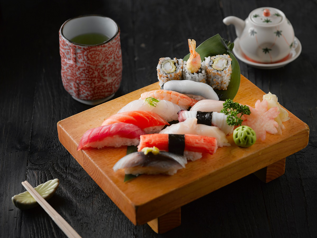 Assorted sushi platter on wooden board paired with green tea and teapot on dark wooden table at Aki Sushi & Asian Fusion, a Sushi Restaurant in Port Washington
