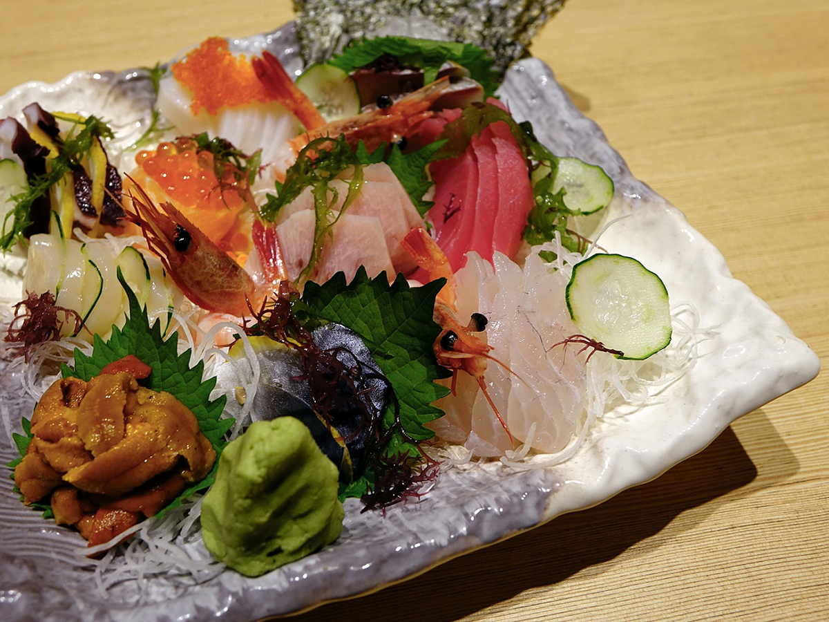 Colorful sashimi combo platter with shrimp, tuna, wasabi and garnishes on textured ceramic dish at Aki Sushi & Asian Fusion, a Sushi Restaurant in Port Washington