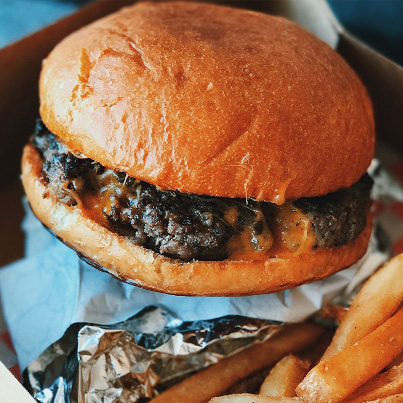 A cheeseburger with melted cheese on a toasted bun served alongside crispy French fries at American wing express, a fast food restaurant in Columbus