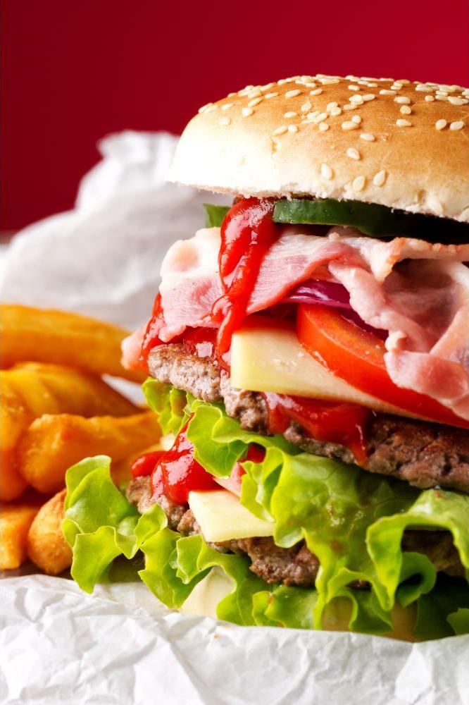 A stacked double beef burger layered with bacon, lettuce, cheese, tomato, and ketchup, served with fries at American wing express, a fast food restaurant in Columbus