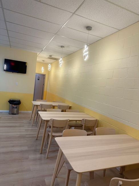 Light wood dining area with tables, chairs, and wall-mounted TV at Asahi Poke & Tea, a Bubble tea store in Beacon