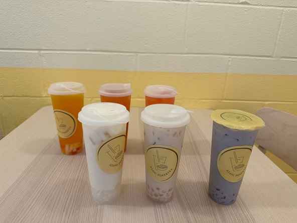 Six assorted bubble tea drinks in branded cups arranged on a table at Asahi Poke & Tea, a Bubble tea store in Beacon