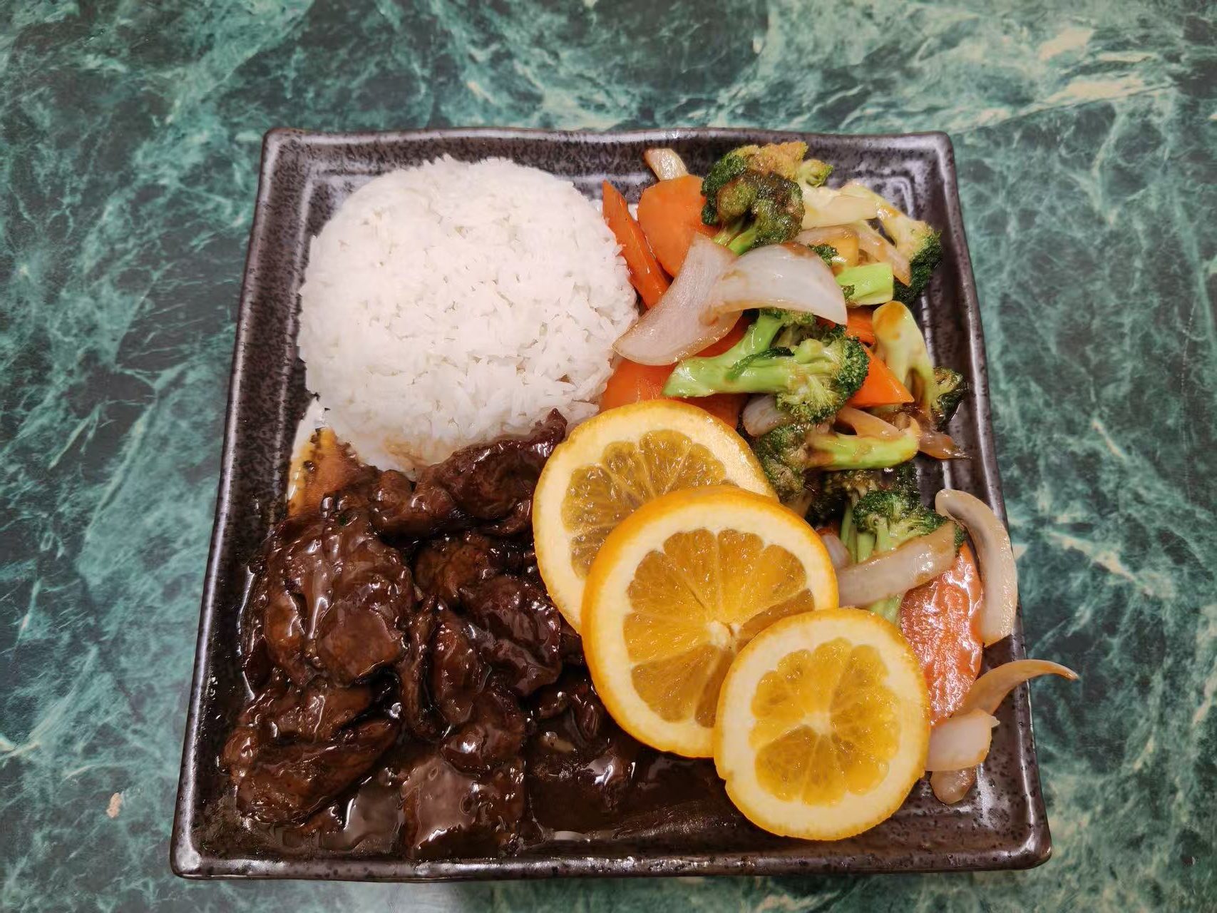 Saucy beef rice plate decorated with orange slices and broccoli veggies at Asia Hibachi & Rice Bowls，an Asian Fusion Restaurant in Buffalo