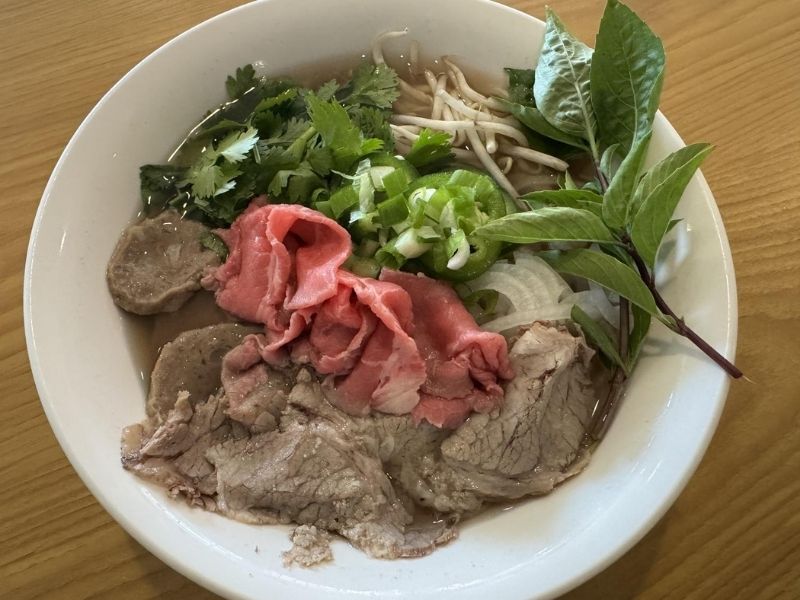 Saigon-Bistro-Vietnamese-Restaurant-Vietnamese-Pho-Savannah A bowl of pho with various meats, herbs, and noodles in a savory broth.
