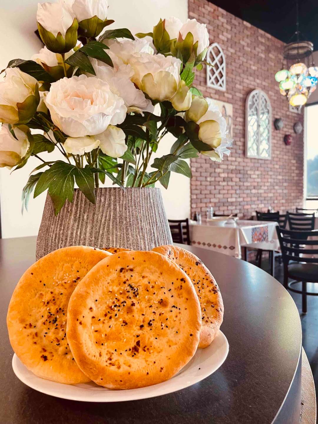 Naan bread presented with a bouquet of flowers in the background at Babahan Uyghur Cafe, a Chinese Xinjiang Flavors Restaurant in Plano