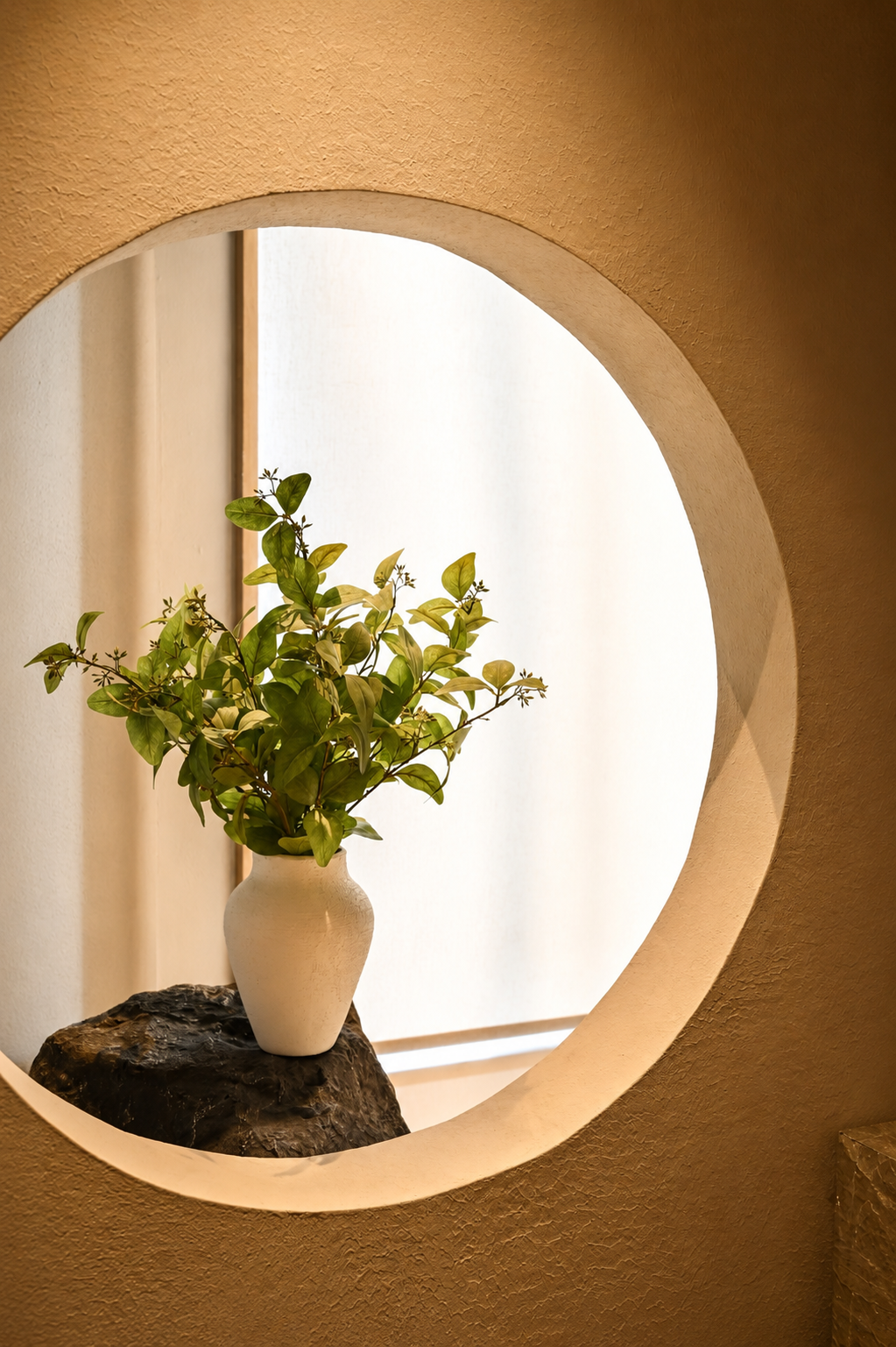 Green leafy arrangement in a white vase displayed inside a softly lit circular wall niche