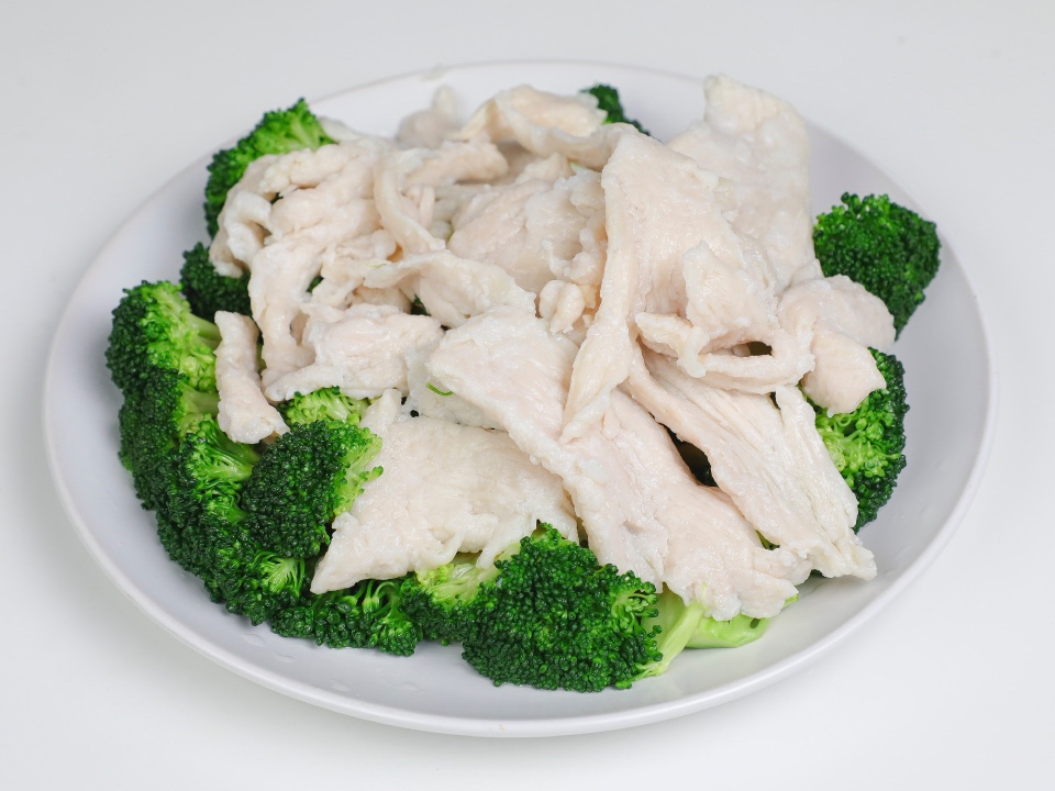 Steamed chicken slices with broccoli on a white plate