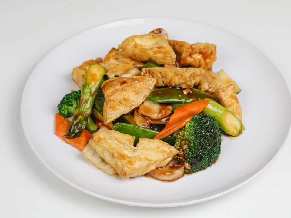 Tofu and vegetable stir-fry in brown sauce on a white plate