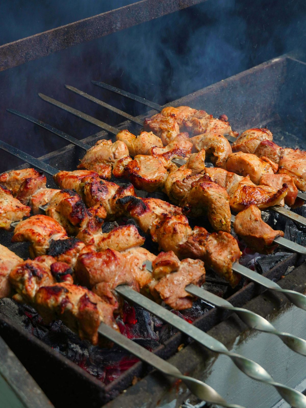 Charred marinated meat skewers grilling over hot charcoal fire at Bk Hand Pulled Noodles, a Chinese Restaurant in Brooklyn