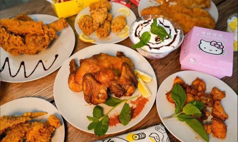 A table spread with roasted whole chicken, fried chicken wings, fried nuggets, and chocolate dessert on white plates at MBL&Q Burger, a Lunch Restaurant in Brooklyn