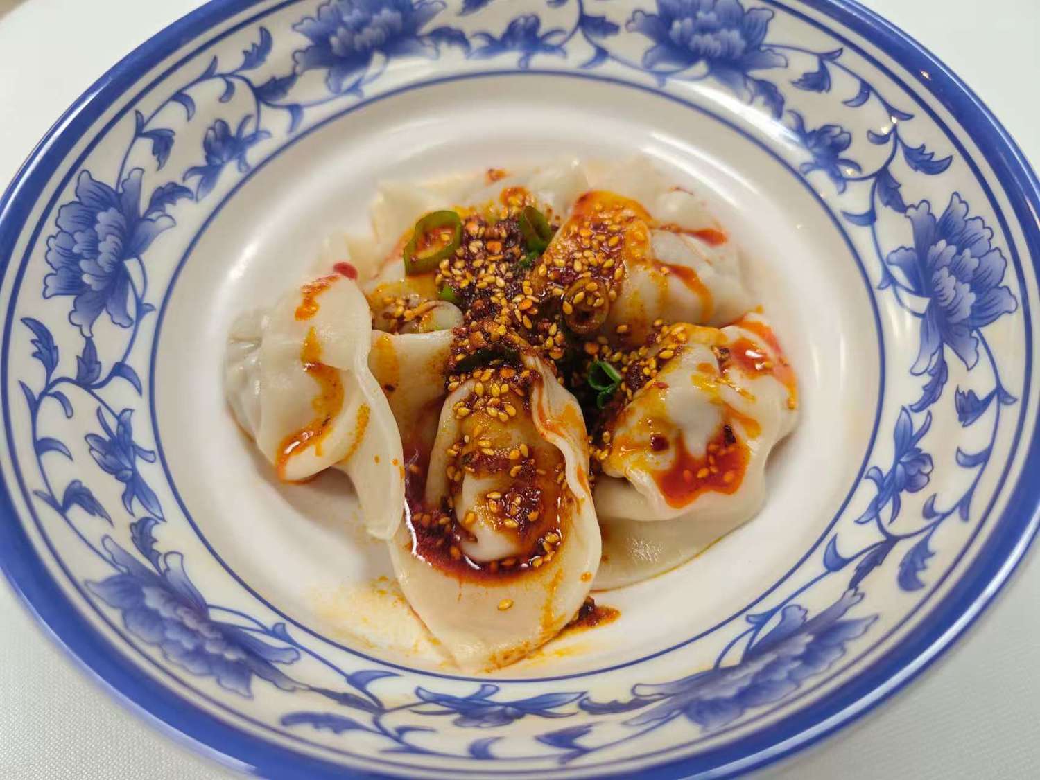 Blue & White-Fried-Rice & Noodles-Asian-Restaurant-Red-Chili-Sauce-Wonton-Las-Vegas Red Chili Sauce Wonton in a blue - and - white porcelain plate. The wontons are plump, drizzled with red oil, and sprinkled with sesame seeds, scallions, etc., looking very appetizing at Blue & White Fried Rice & Noodles,a Asian Restaurant in Las Vegas