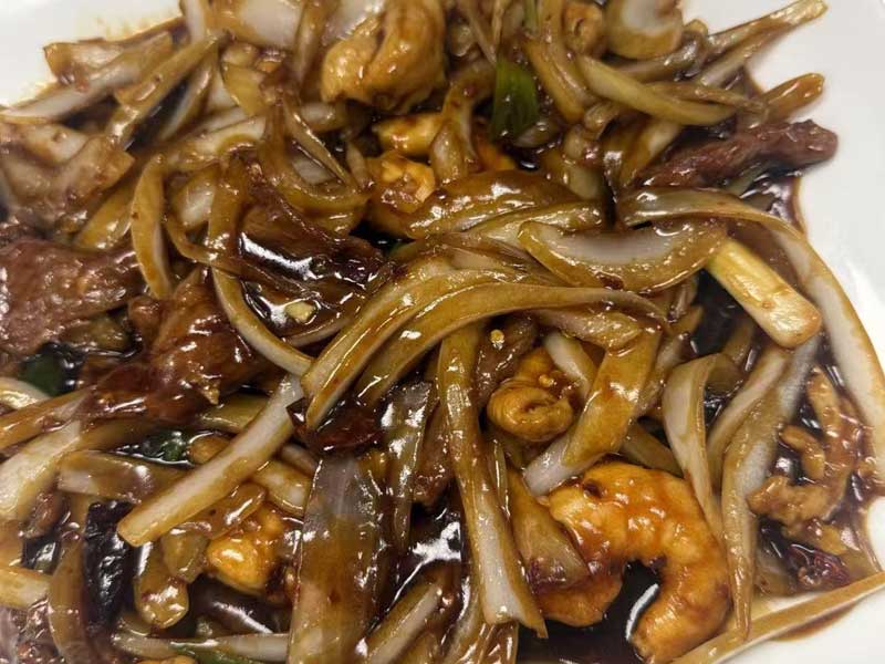 Stir‑fried mixed seafood, beef and sliced onion coated in glossy dark brown savory sauce, served on white round ceramic plate.