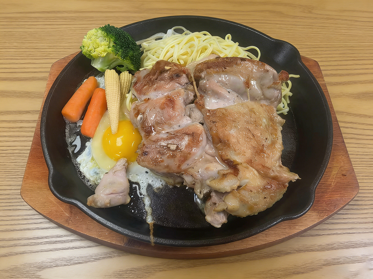 Grilled chicken steak with spaghetti, fried egg and vegetables on a black iron plate at Bull King Steak House，a Asian Fusion Steakhouse in Glendale