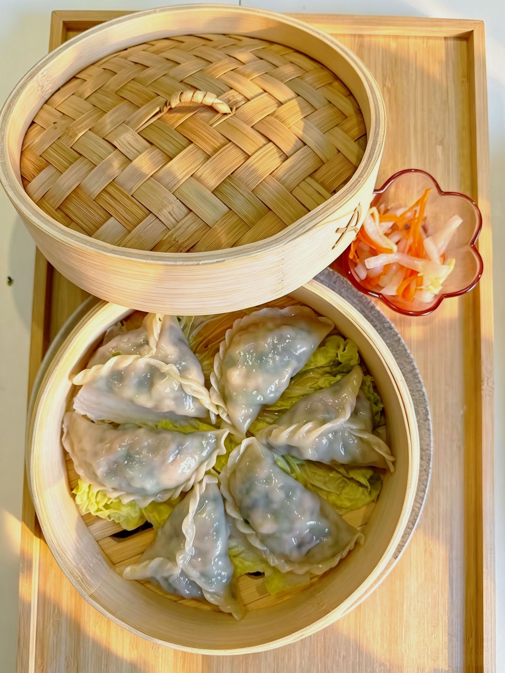 Clear overhead shot of steamed dumplings inside bamboo steamer with pickled carrot radish slaw at Cafe On Seneca, an Asian Fusion Restaurant in Ridgewood