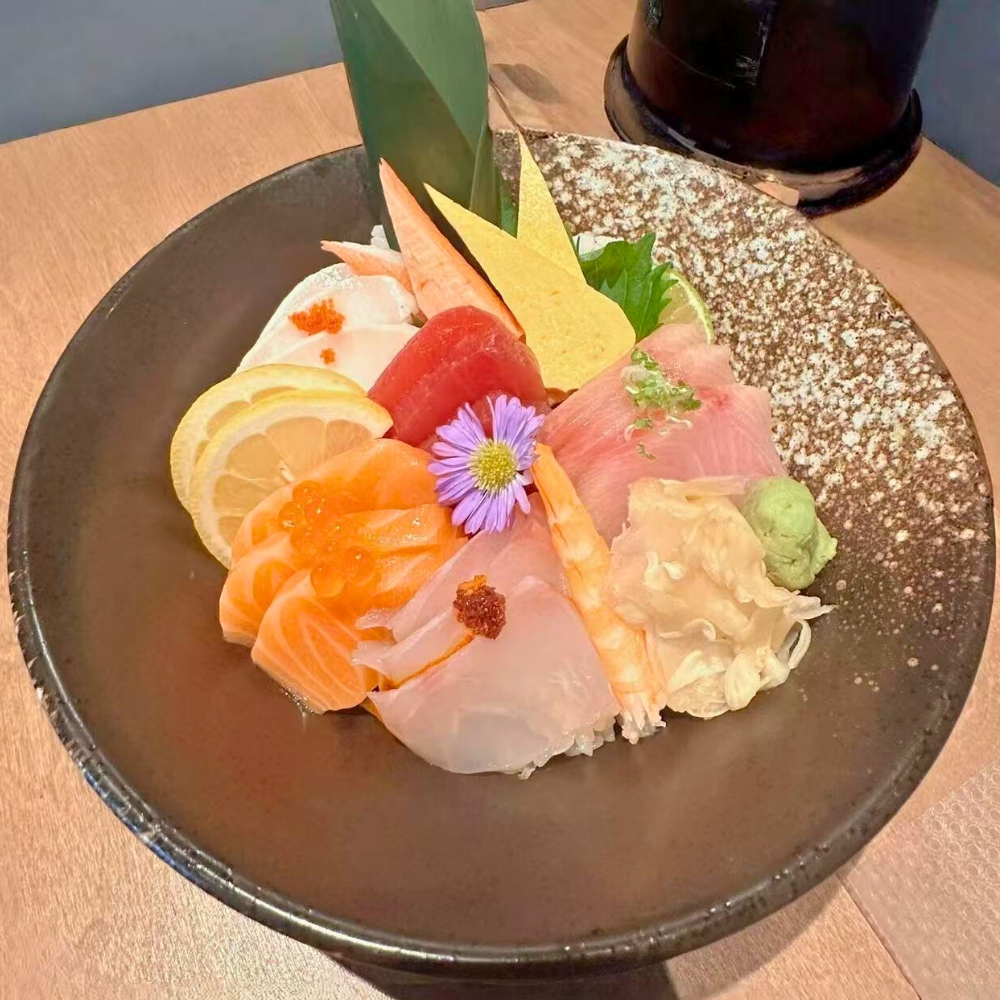 Assorted fresh sashimi over sushi rice, garnished with lemon and edible flower at Catzuneko Shokudo, a Japanese Restaurant in New York