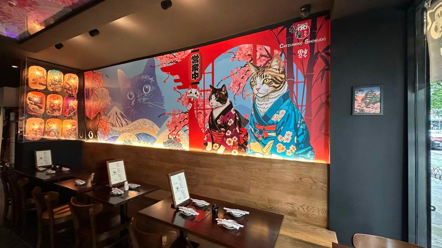 Interior dining area with Japanese cat mural, lanterns, and wooden tables at Catzuneko Shokudo, a Japanese Restaurant in New York