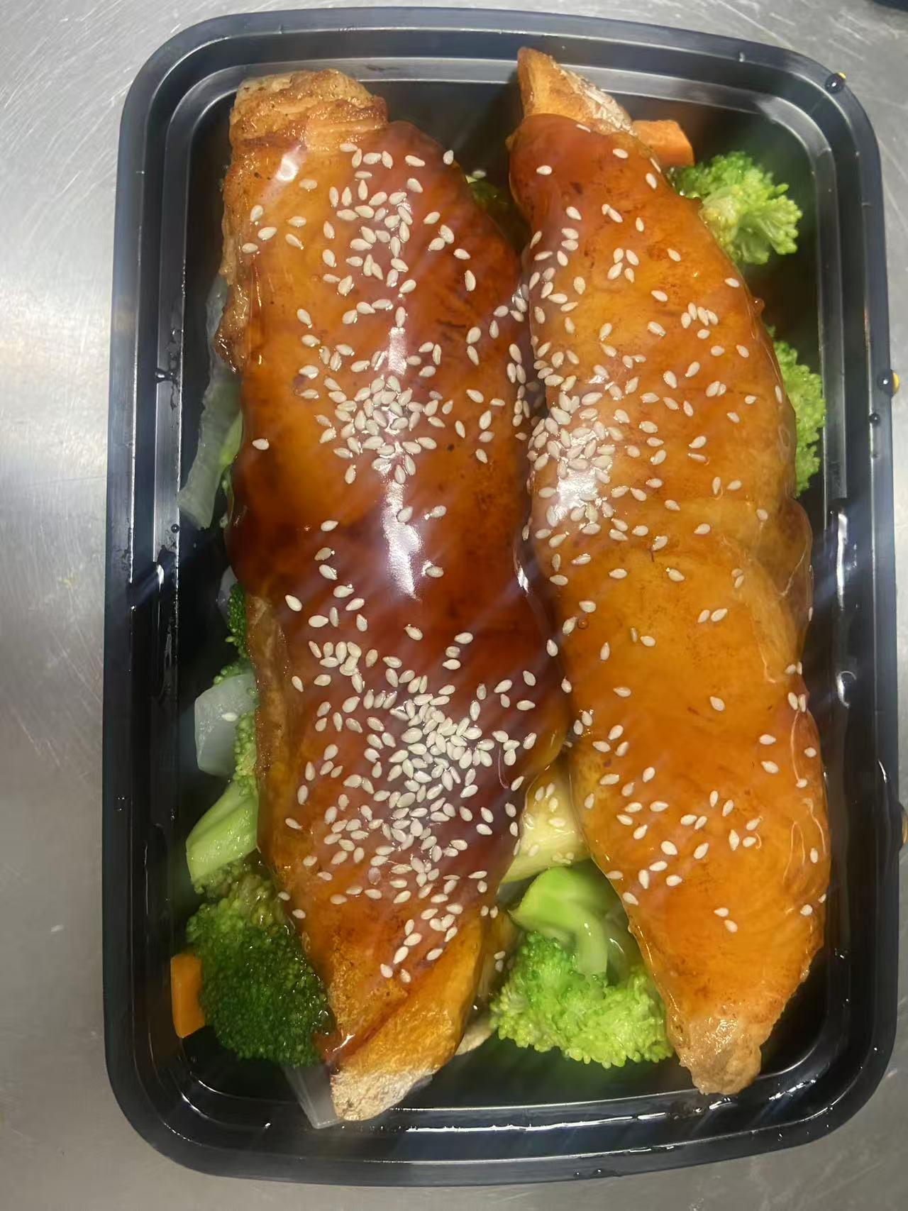 Two sesame-glazed fish fillets over broccoli in a black takeout container