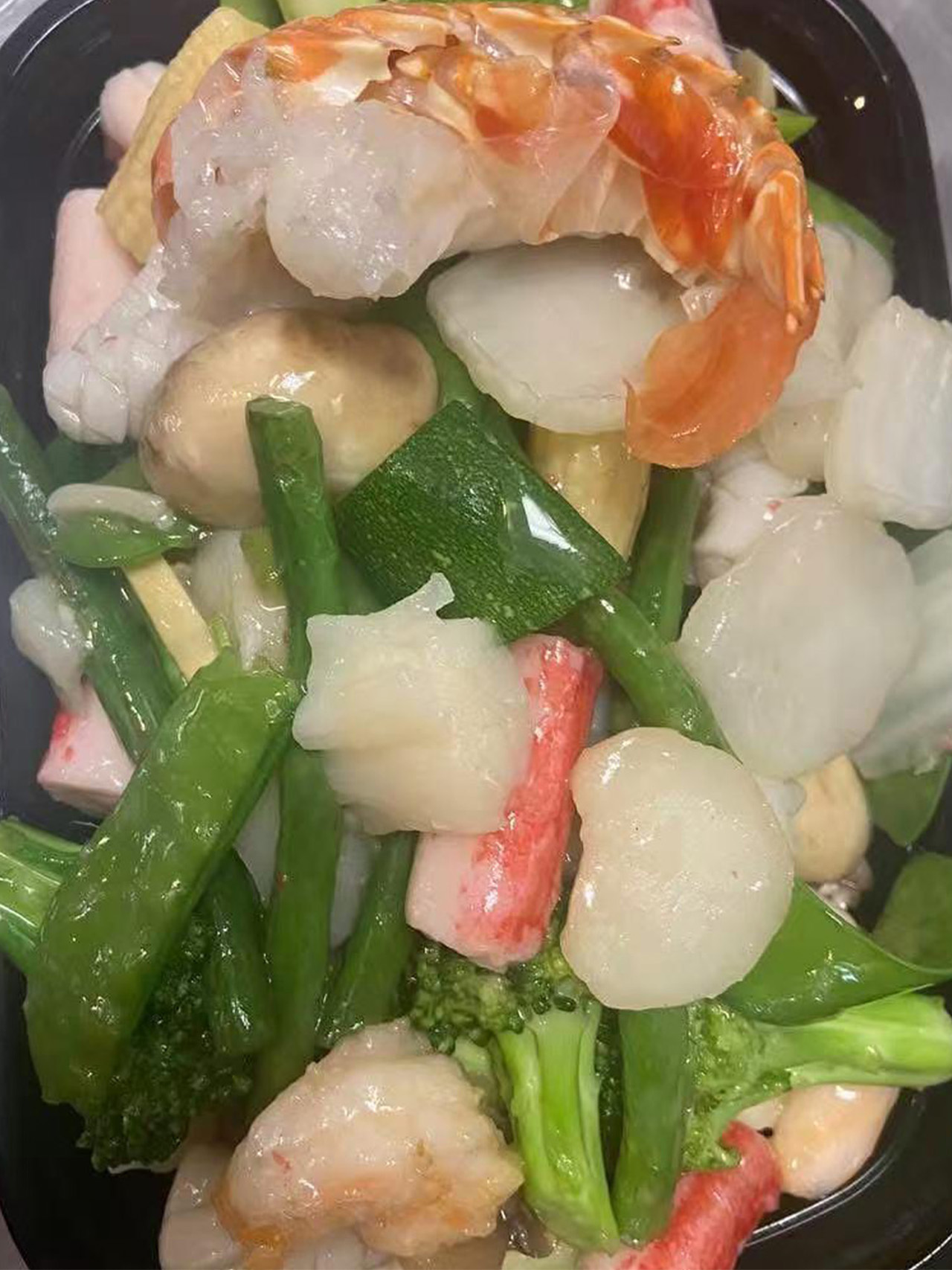 Seafood Delight with shrimp, crab stick, scallops, and greens in a takeout box