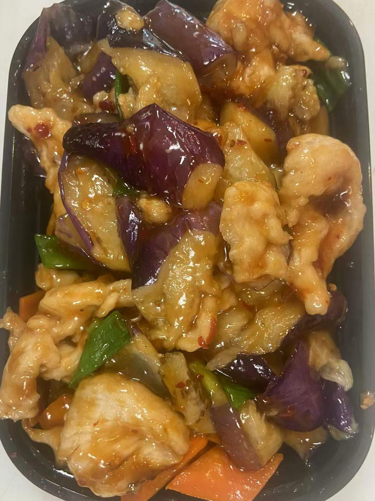 Stir-fried eggplant, chicken, and green peppers in a black takeout container