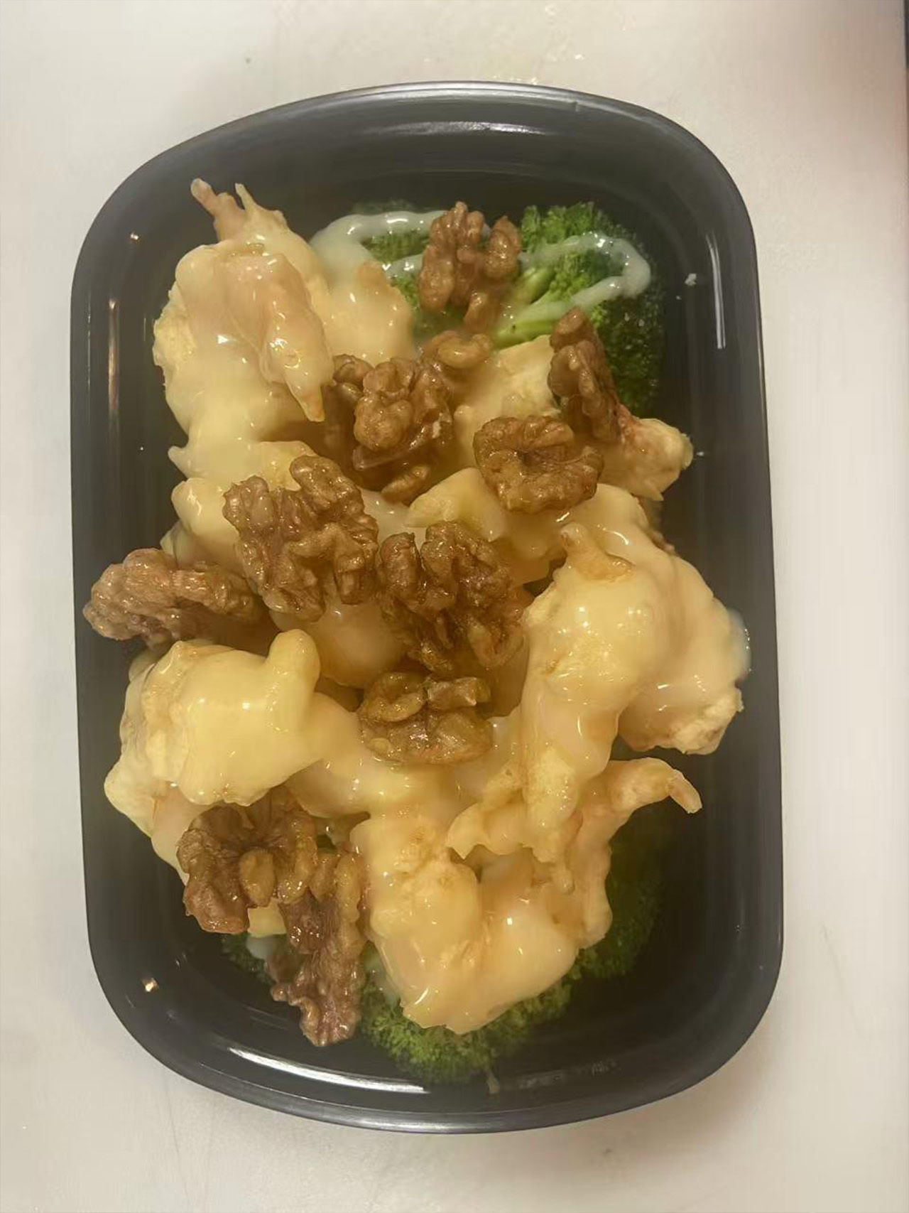 Creamy shrimp with candied walnuts over broccoli in a black takeout container