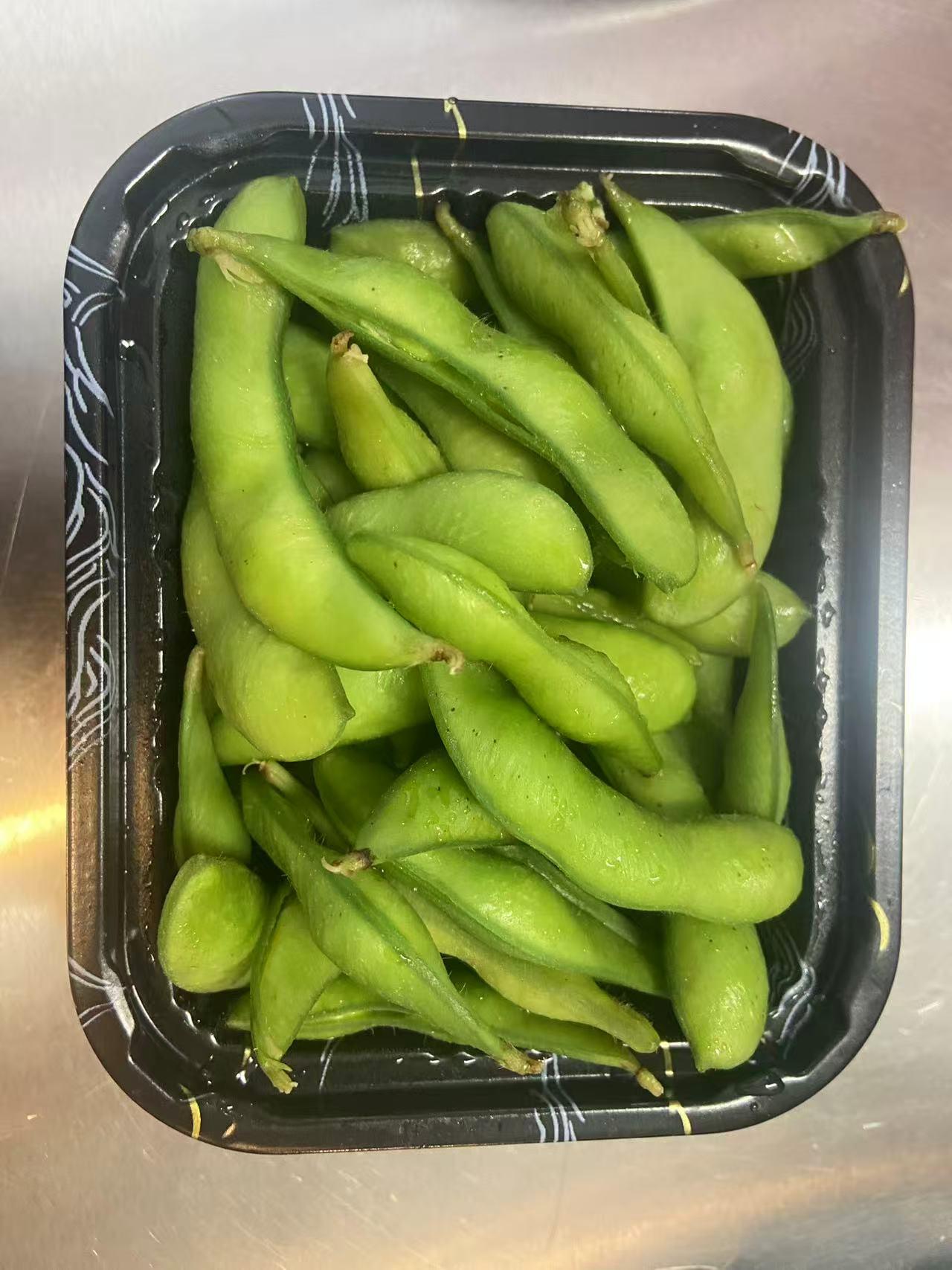 Boiled edamame pods in a black takeout container