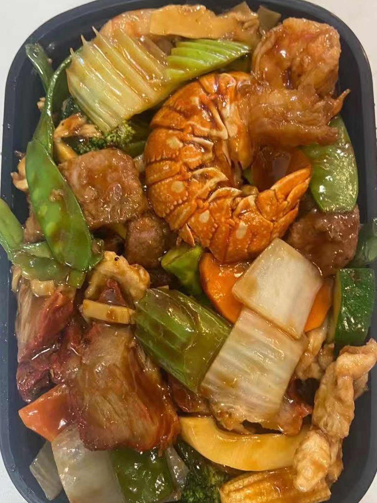 Happy family stir-fry with lobster, shrimp, chicken, and mixed vegetables in a takeout box