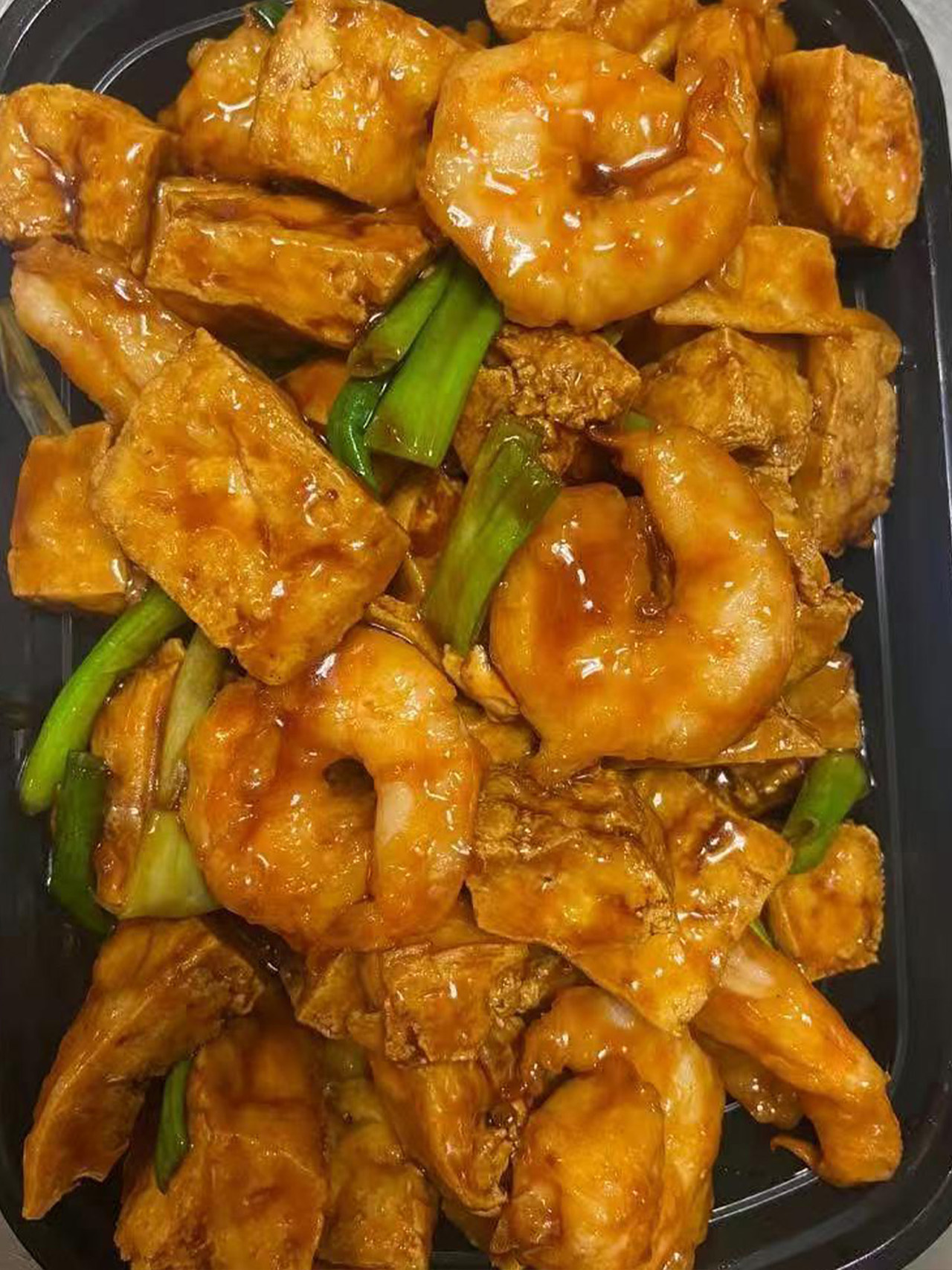 Shrimp and crispy bean curd with scallions in a brown sauce in a takeout box