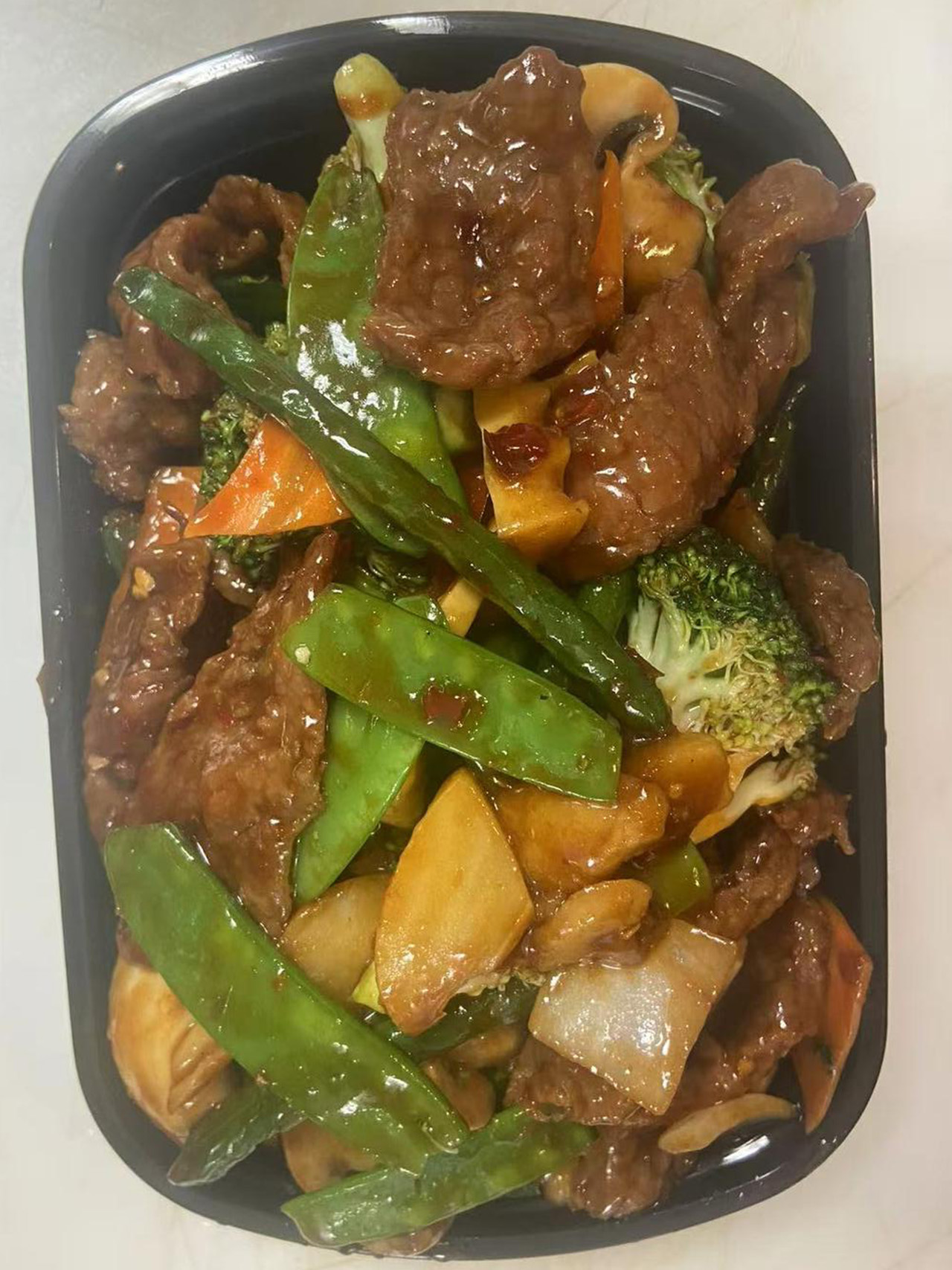 Beef stir-fry with snow peas, broccoli, and carrots in a takeout box.