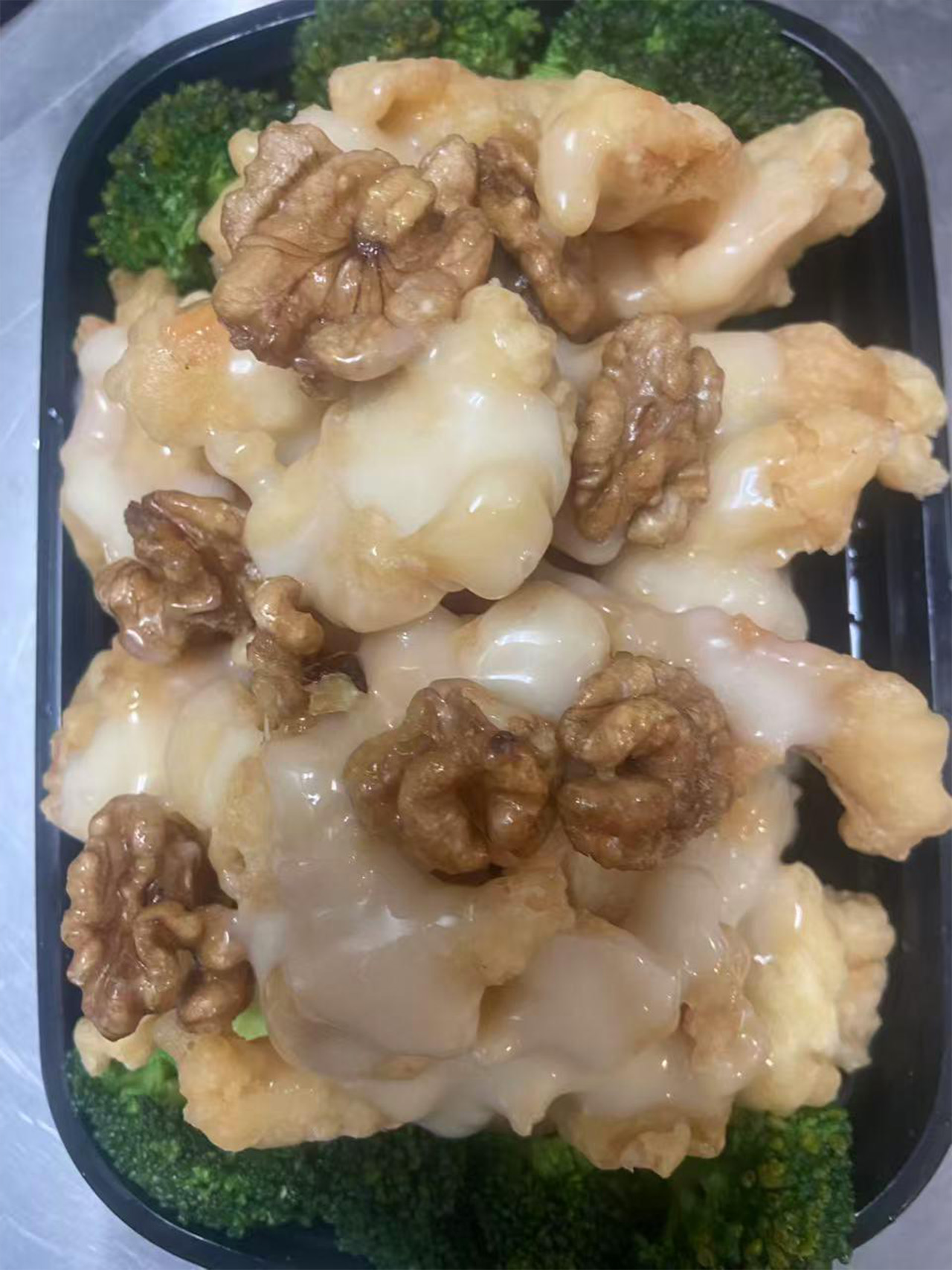 Walnut shrimp with creamy sauce over broccoli in a takeout box