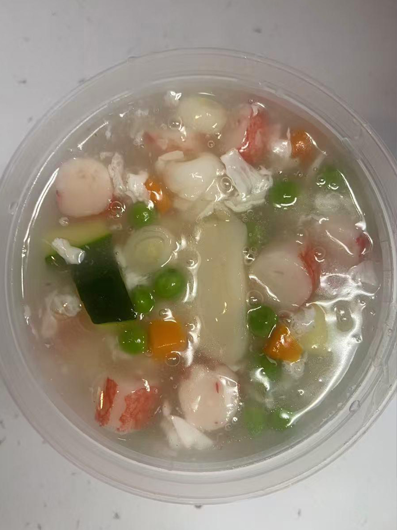 Clear seafood soup with fish balls, crab sticks, and peas